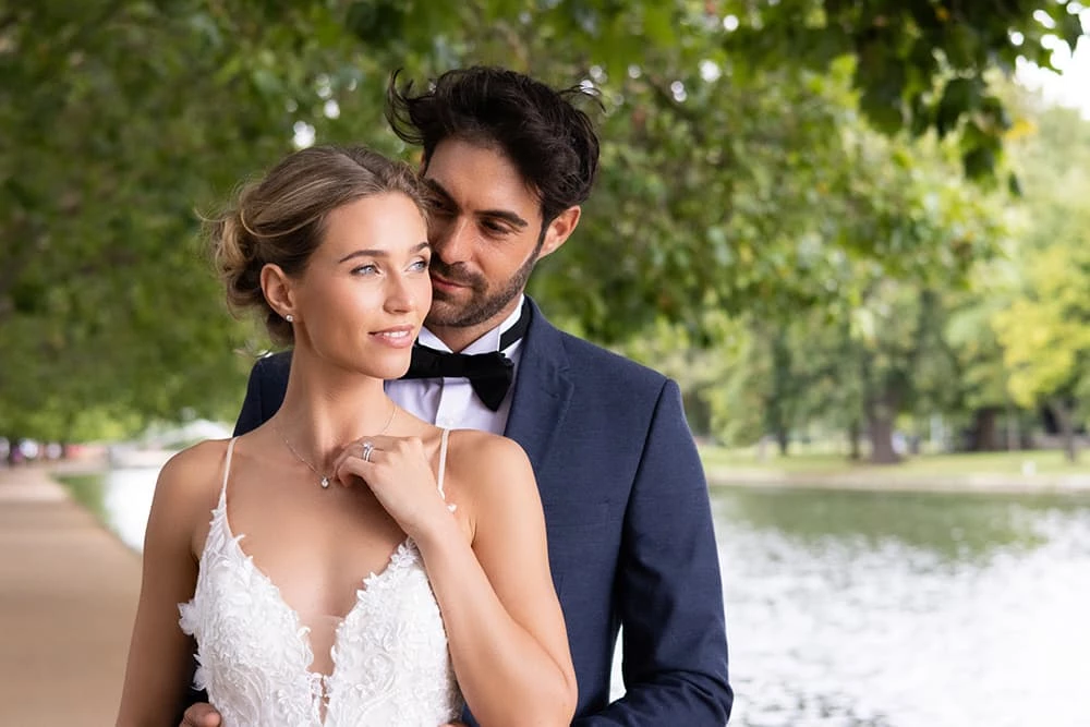 A bride and groom standing by a river in Bedford wearing Baker Brothers jewellery