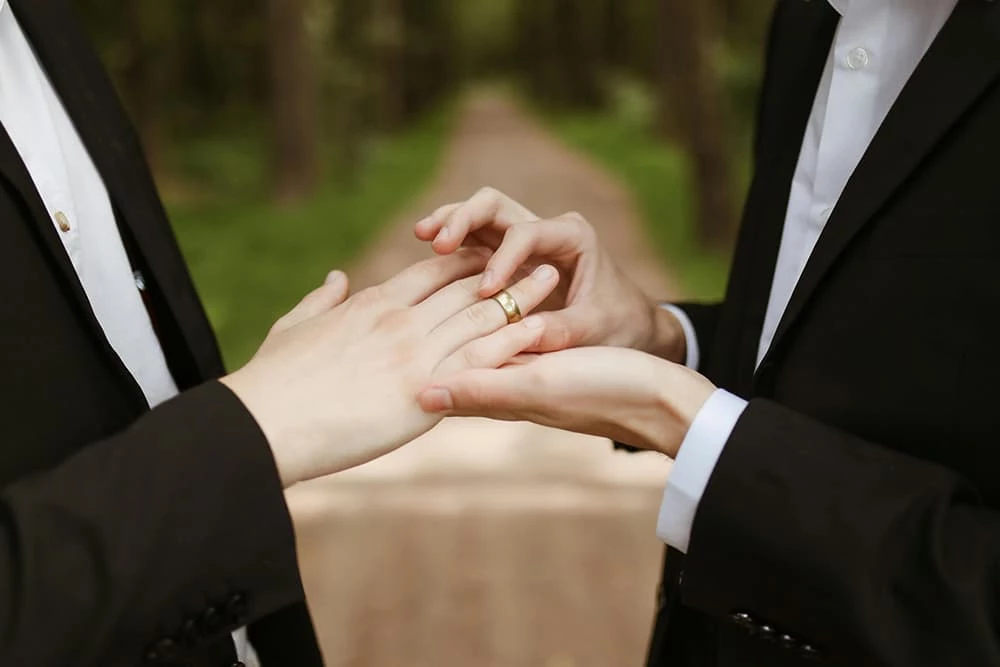 A groom putting a wedding ring on another groom